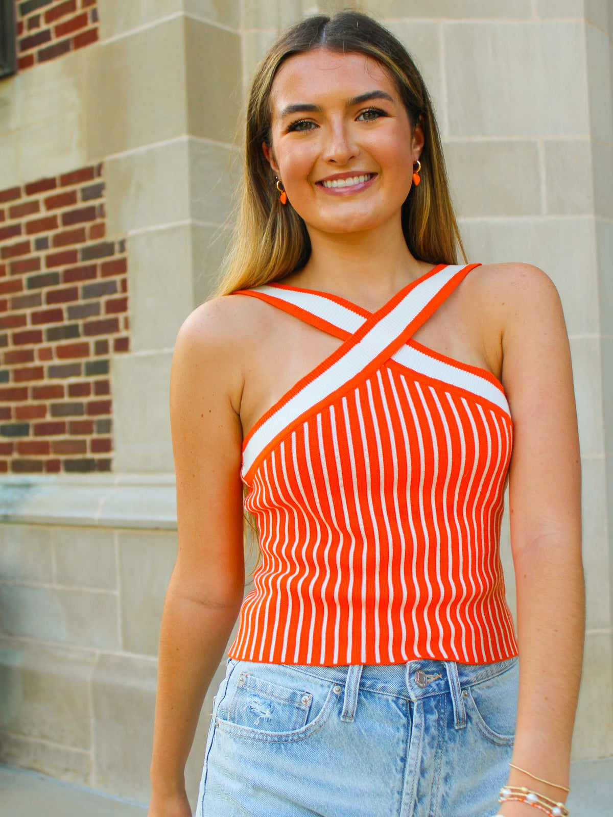 Woman wearing a red and white striped top with blue jeans standing in front of a brick wall.