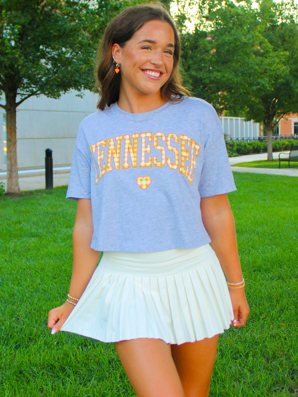 Woman wearing a blue 'Tennessee' t-shirt and white skirt outdoors.