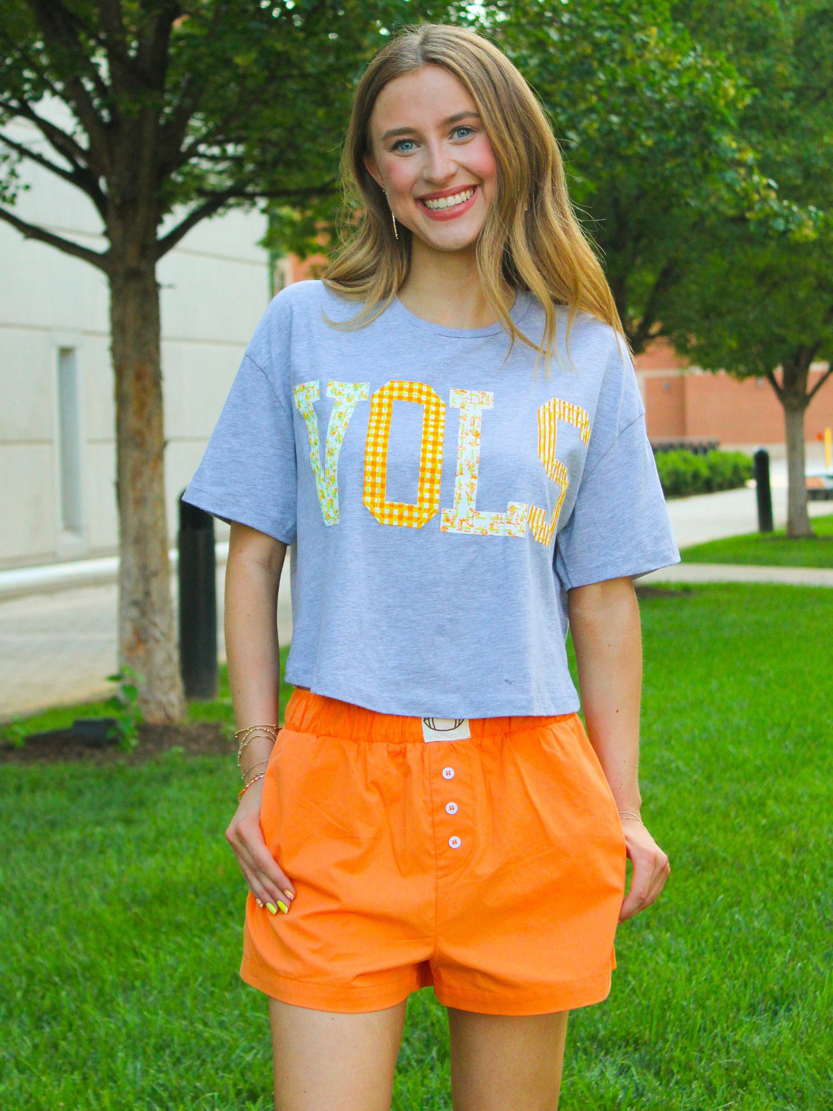 Woman wearing a light blue t-shirt with 'VOLS' and orange shorts outdoors.