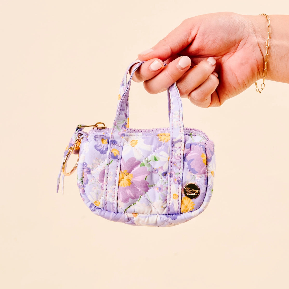 Hand holding a Purple Floral Mini Duffle Bag Bag Charm on Cream Background Darling Effect Itty Bitty Duffle Bag Charm Bouquet Beauty Purple