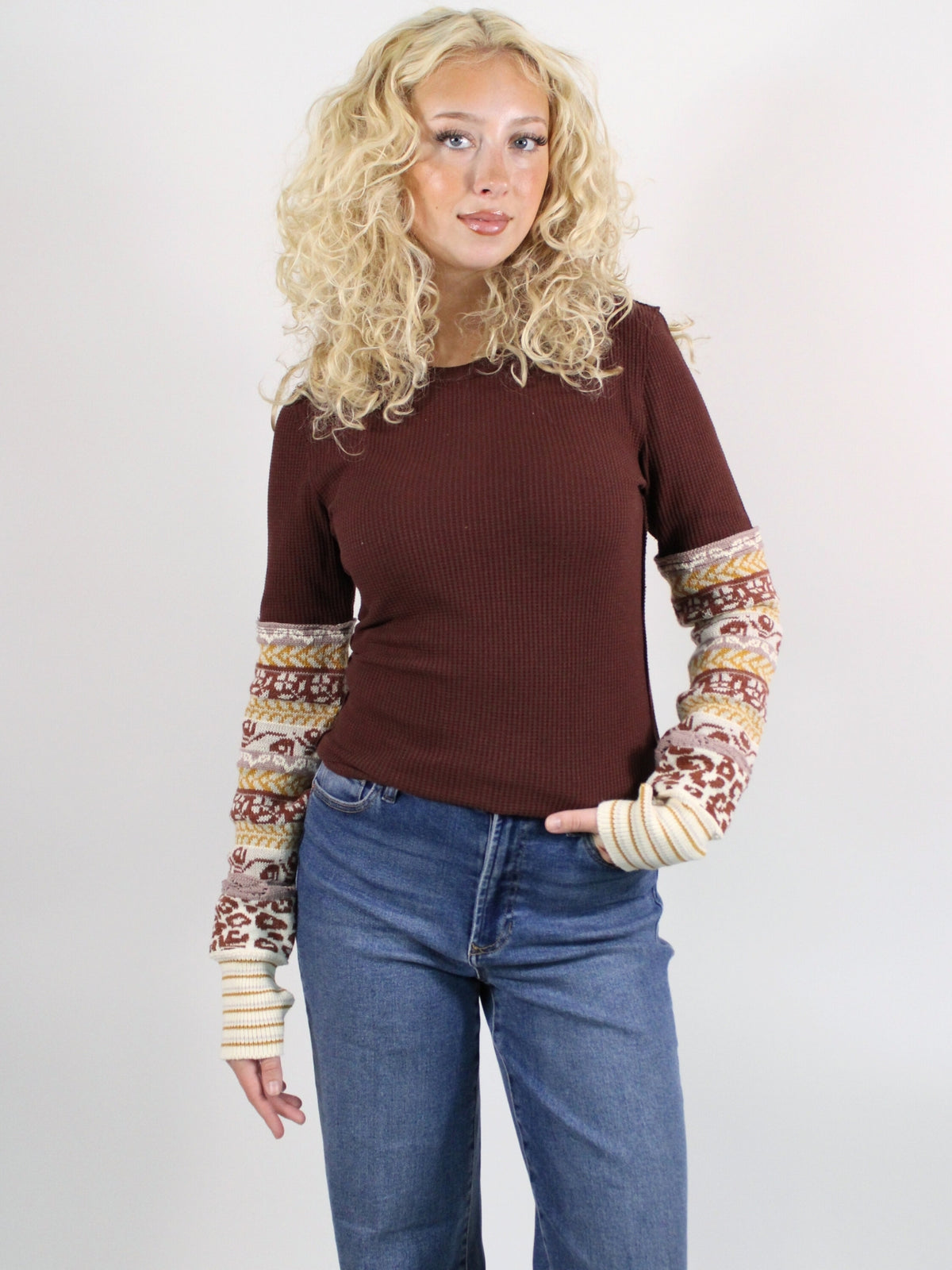 Woman wearing a brown sweater with patterned sleeves against a white background
