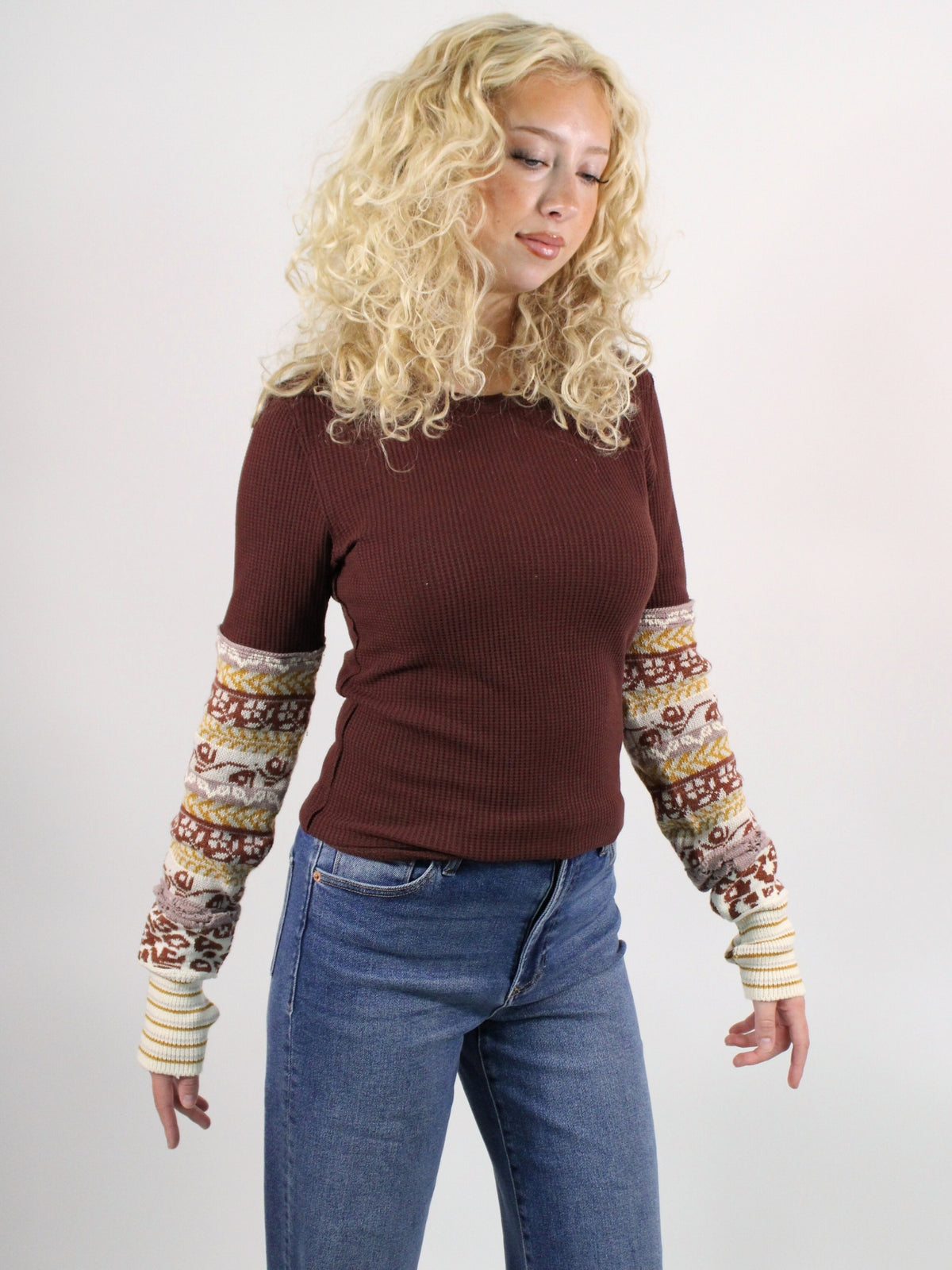 Woman wearing a brown ribbed sweater with patterned sleeves against a plain background