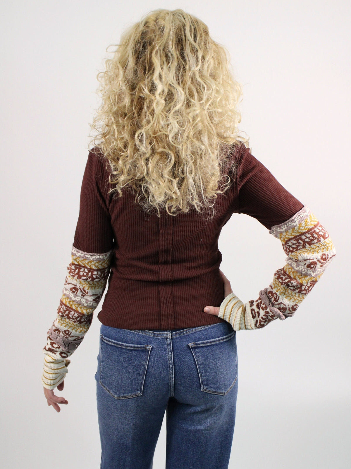 Person wearing a brown sweater with patterned sleeves on a white background