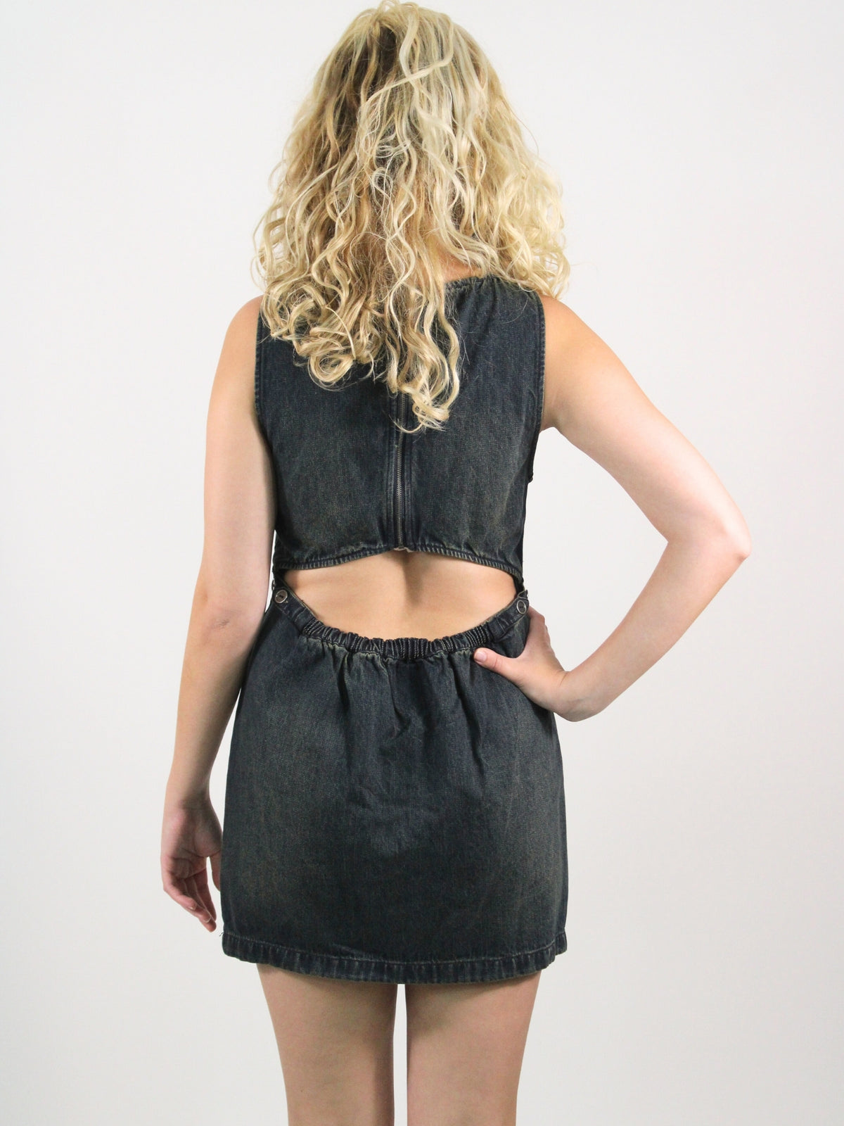 Person wearing a black denim dress with cut-out back on a white background