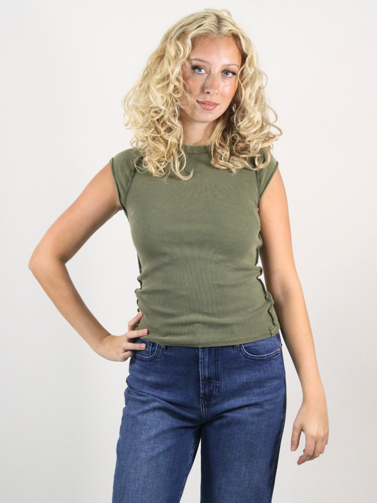 Woman wearing a green sleeveless top and blue jeans against a white background