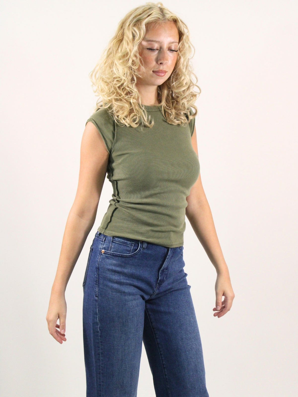 Woman wearing an olive green sleeveless top and blue jeans on a white background