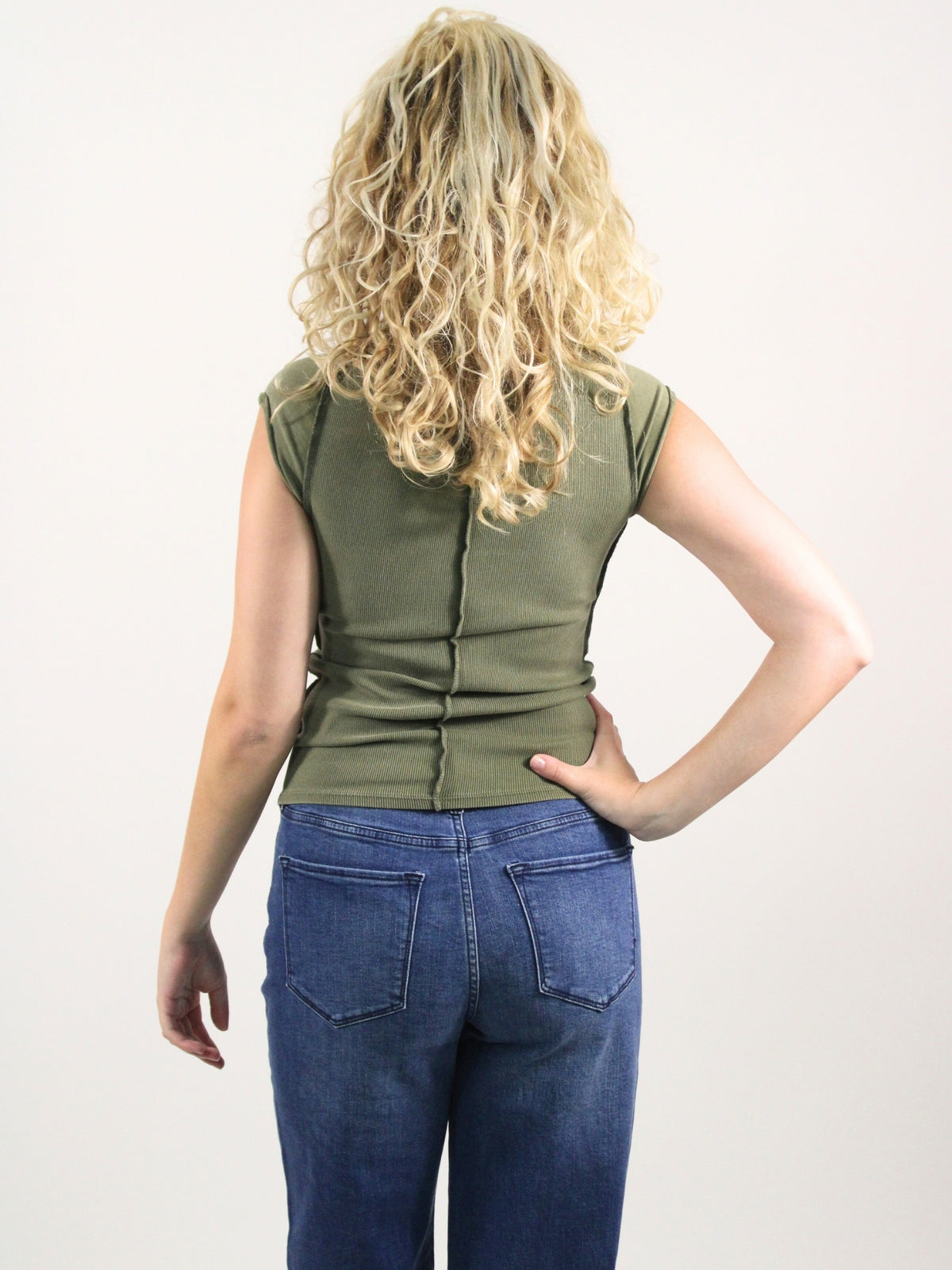 Person wearing an olive green sleeveless top and blue jeans on a white background