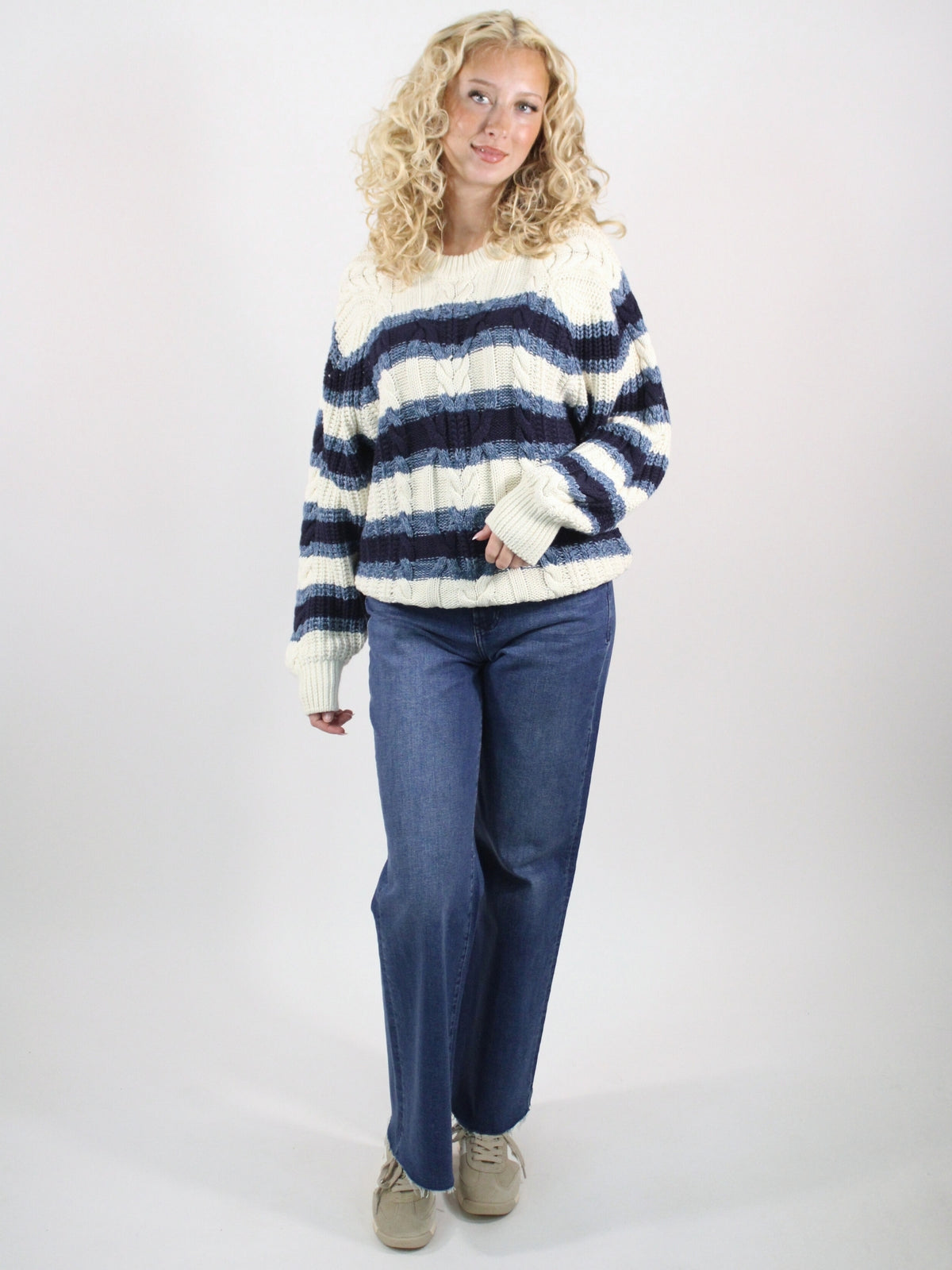 Woman wearing a striped sweater and blue jeans on a white background