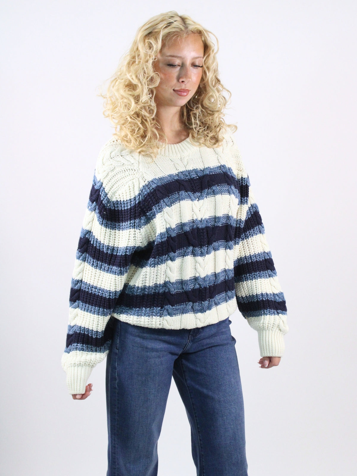 Woman wearing a white and blue striped sweater with blue jeans on a white background