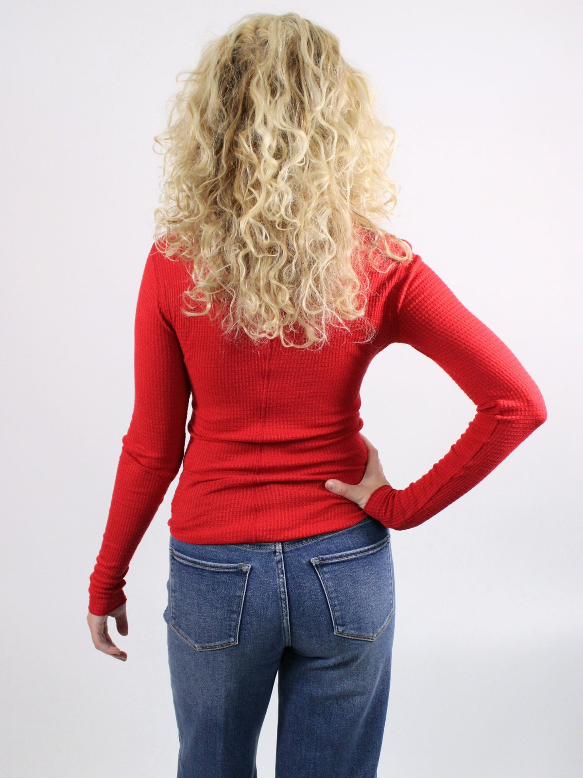 Woman wearing a red long-sleeve top and blue jeans on a white background
