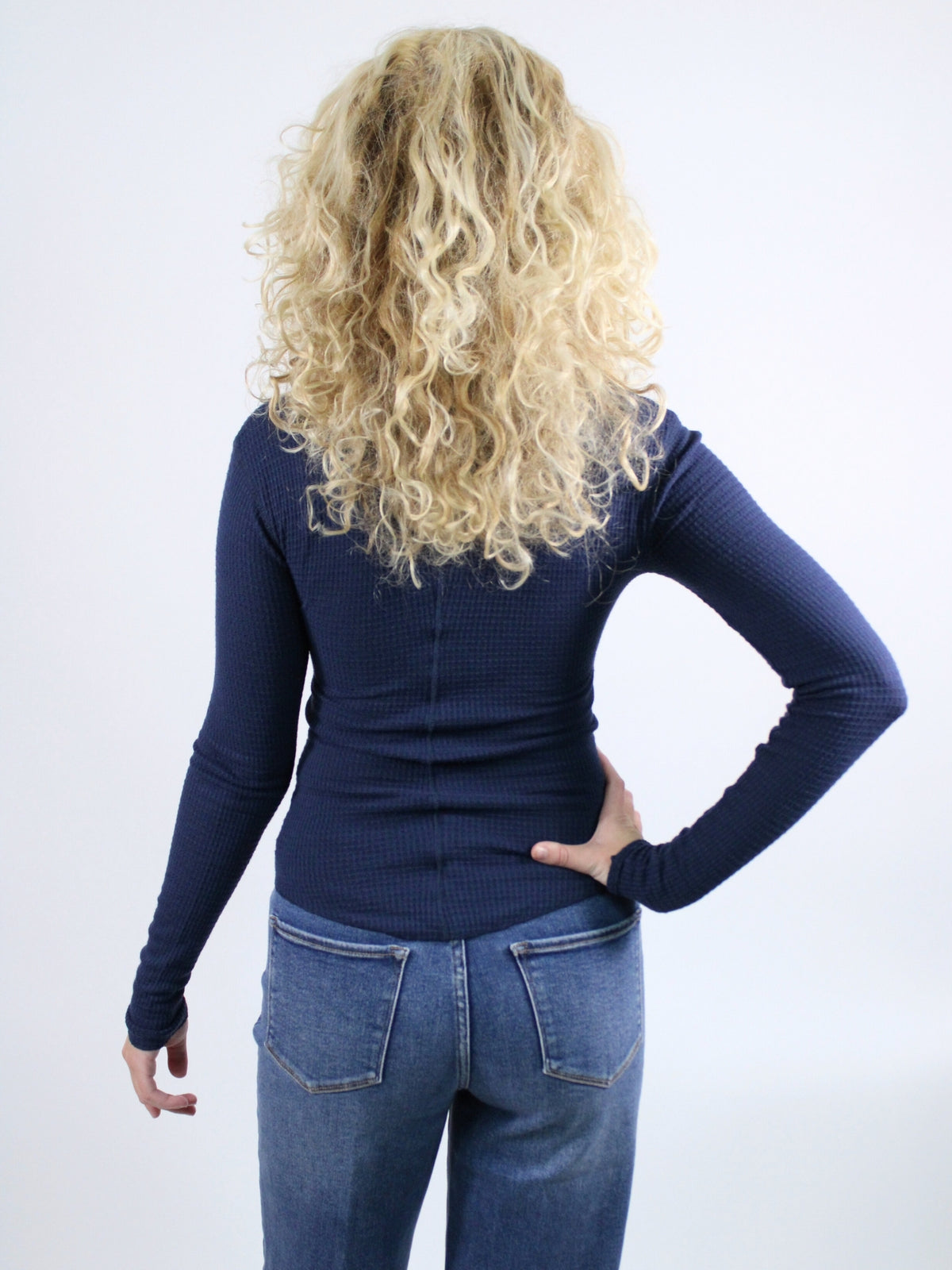 Woman wearing a navy blue long-sleeve button-up shirt and blue jeans against a white background
