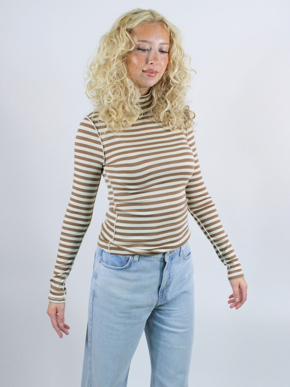 Woman wearing a striped long-sleeve top and light blue jeans against a white background