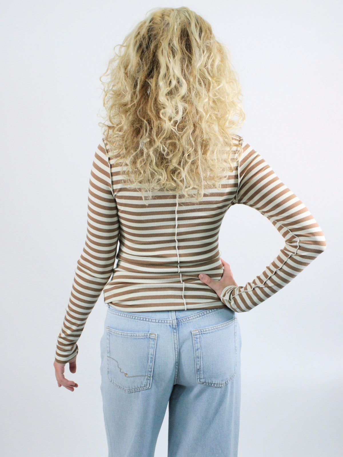 Person wearing a striped long-sleeve shirt and light blue jeans on a white background