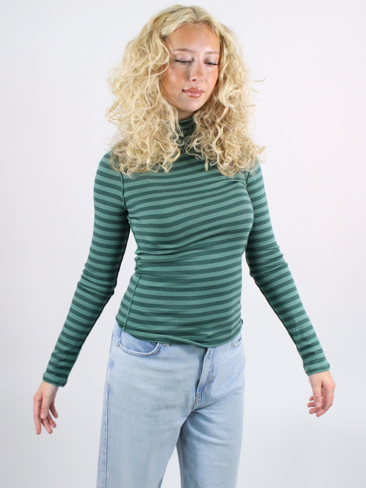Woman wearing a green striped turtleneck and light blue jeans on a white background