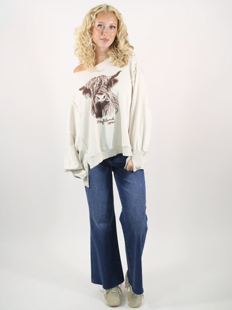 Woman wearing a white sweater with a cow graphic and blue jeans on a white background