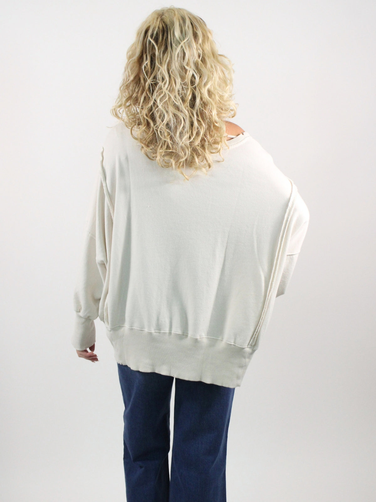 Person wearing a white sweatshirt and blue pants on a plain background