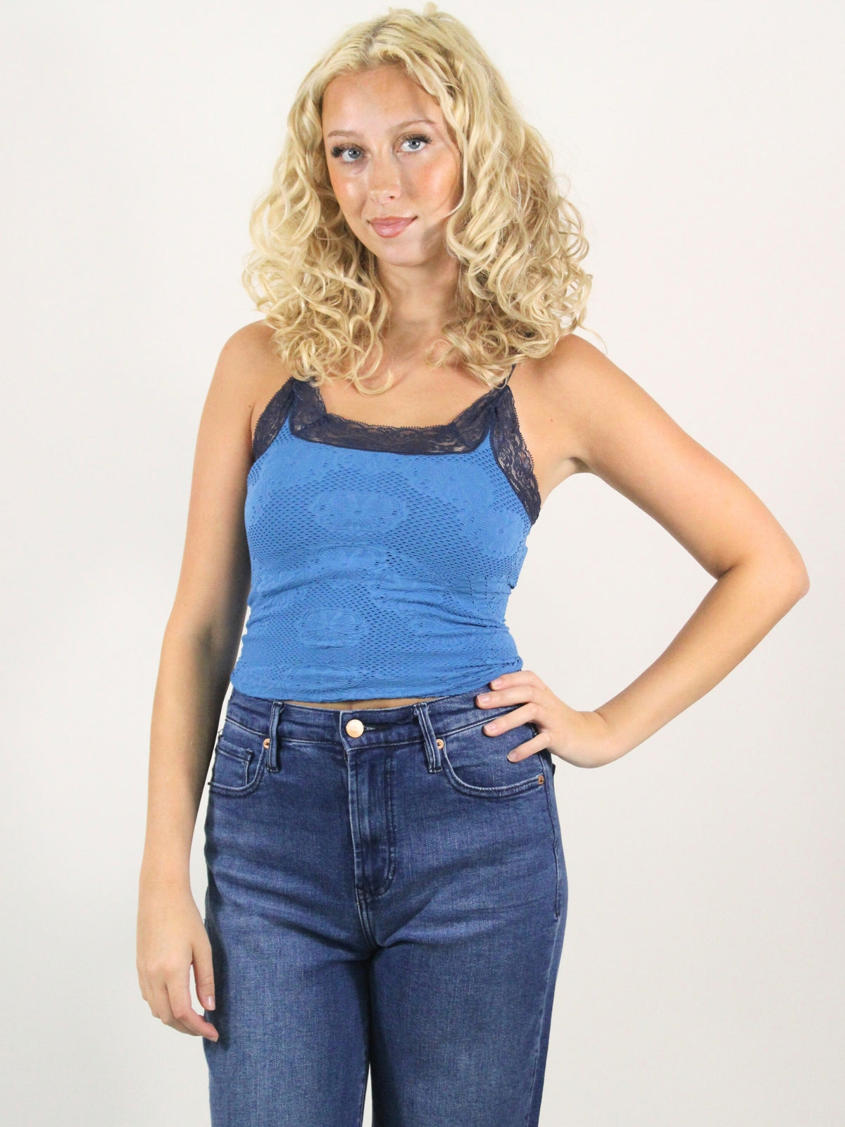 Woman wearing a blue lace top and jeans against a white background