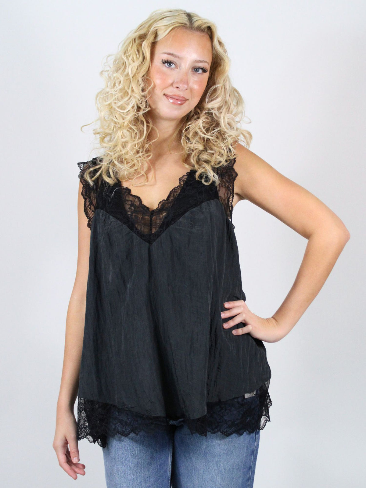 Woman wearing a black lace top and blue jeans against a white background