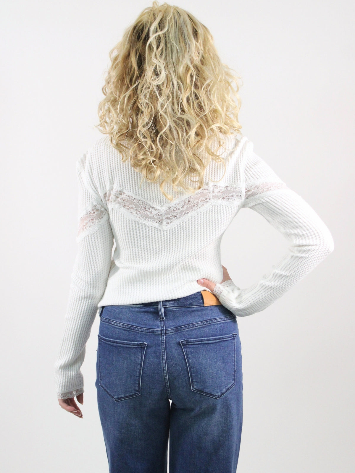 Person wearing a white sweater with lace details and blue jeans on a plain background