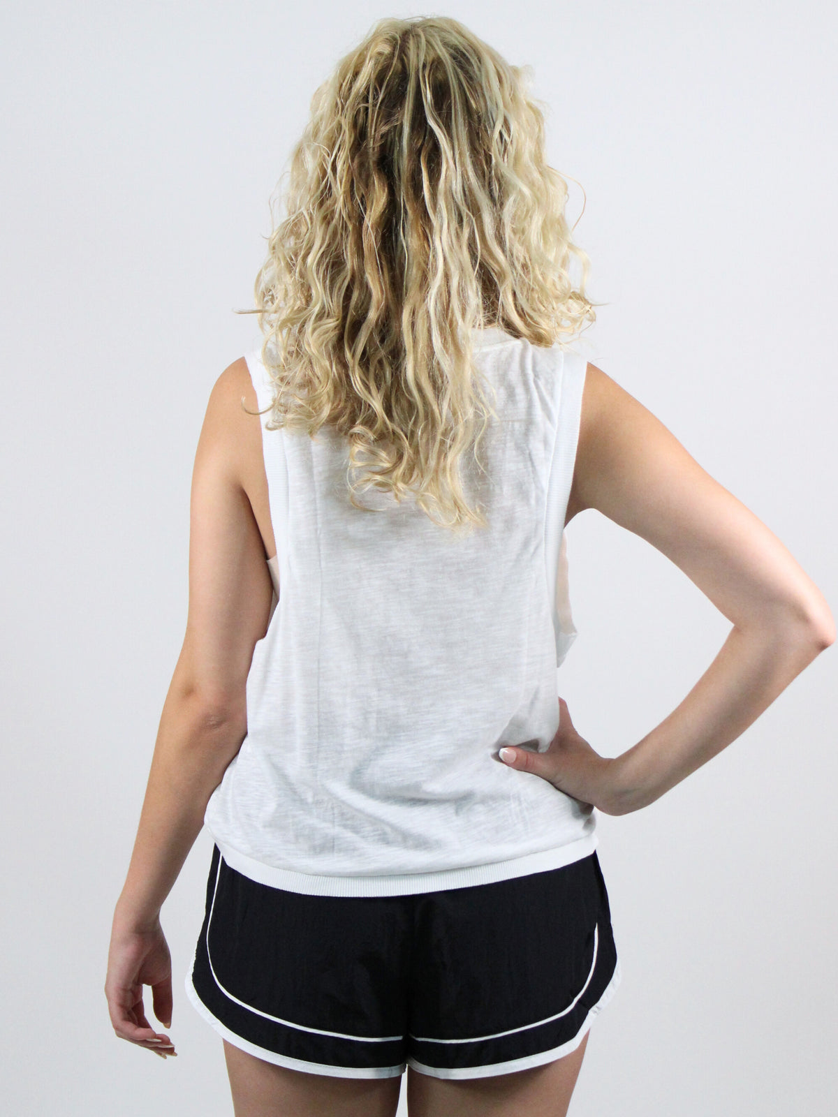 Person wearing a white sleeveless top and black shorts on a plain background