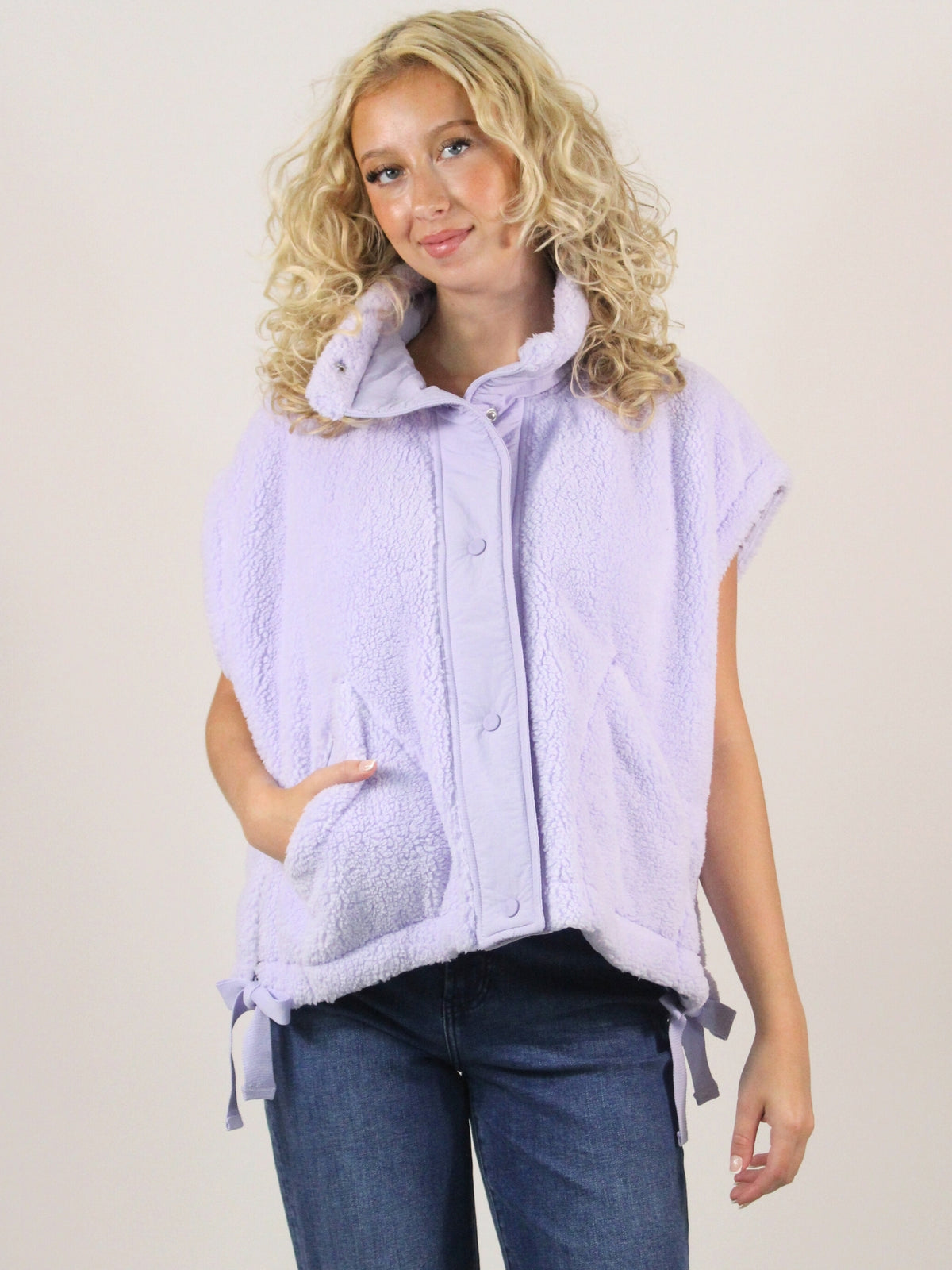 Woman wearing a light purple vest with a white collar against a plain background