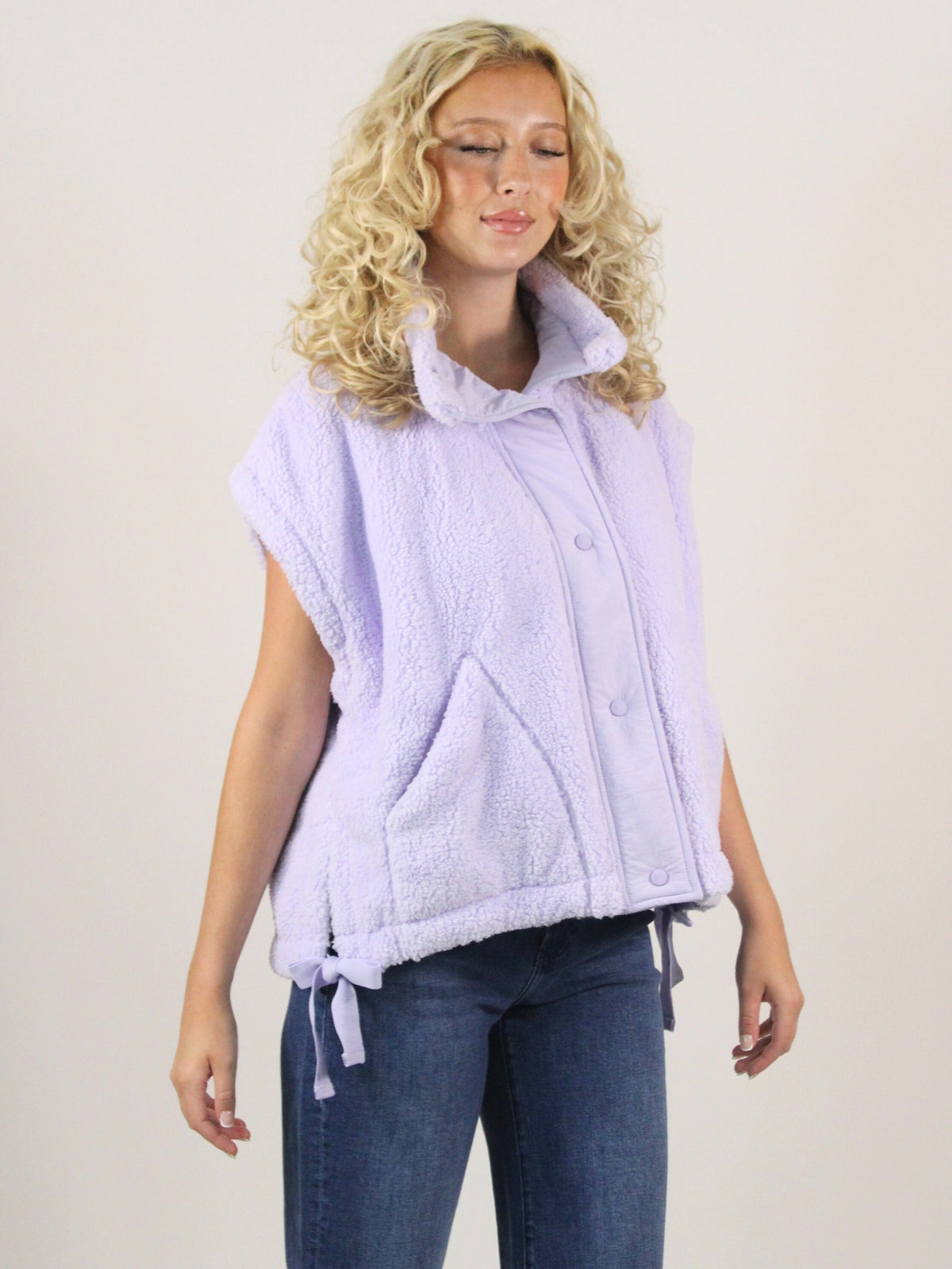Woman wearing a light purple vest over a shirt with blue jeans on a plain background