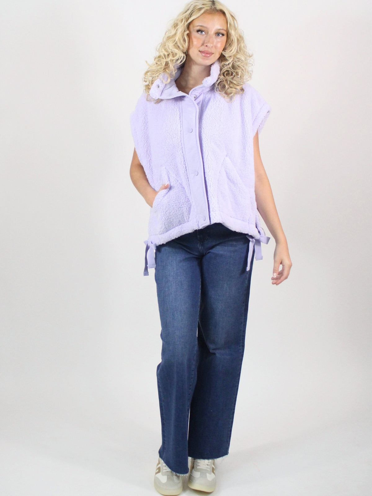 Woman wearing a light purple vest over a white shirt with blue jeans on a white background