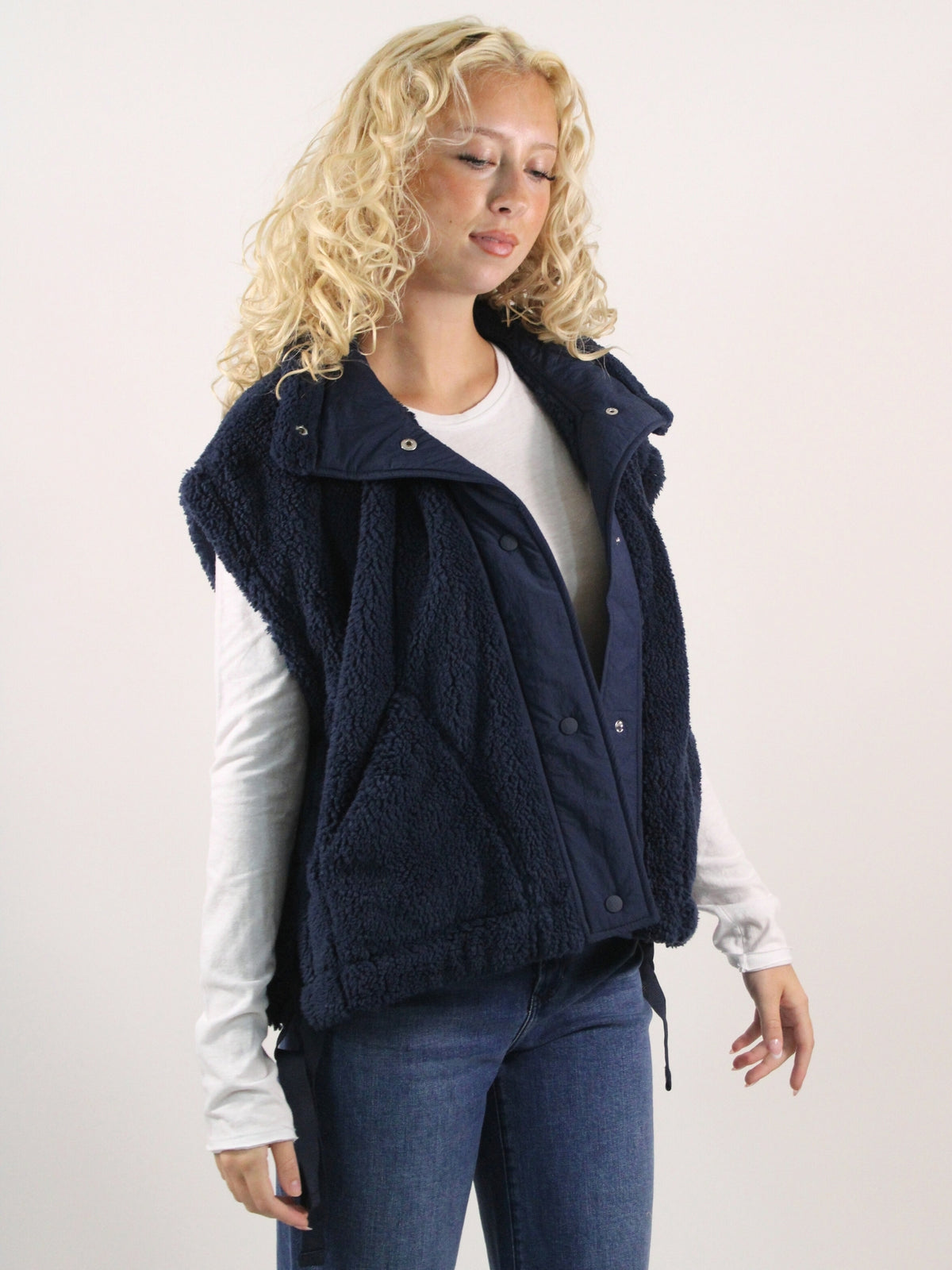 Woman wearing a navy blue vest over a white shirt and blue jeans on a light background