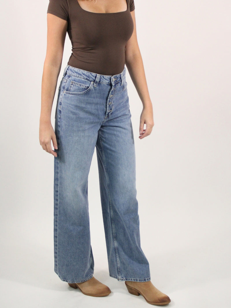 Person wearing a brown top and blue jeans on a plain background