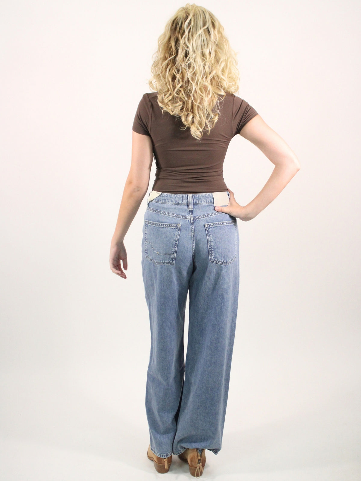 Person wearing a brown shirt and blue jeans on a white background
