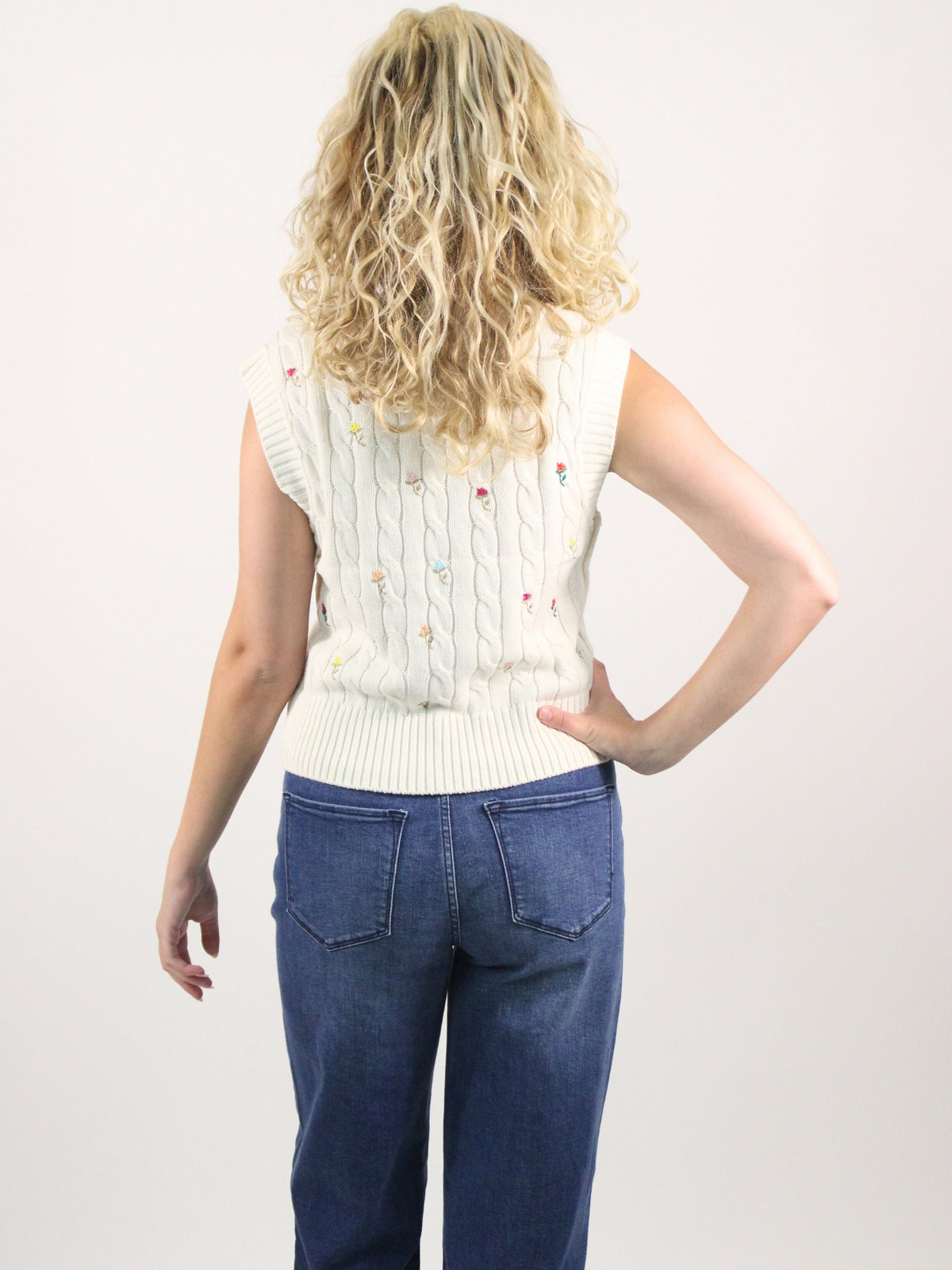 Person wearing a white knitted vest and blue jeans on a plain background