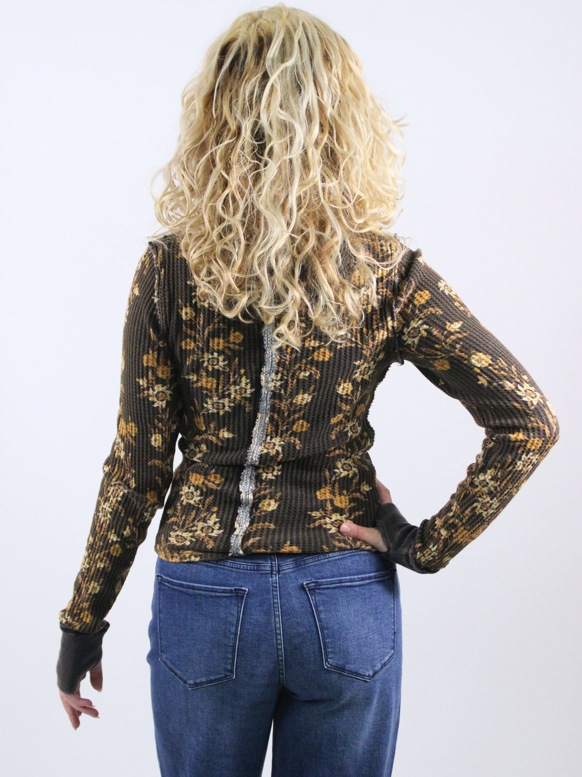 Person wearing a patterned long-sleeve top and blue jeans on a white background