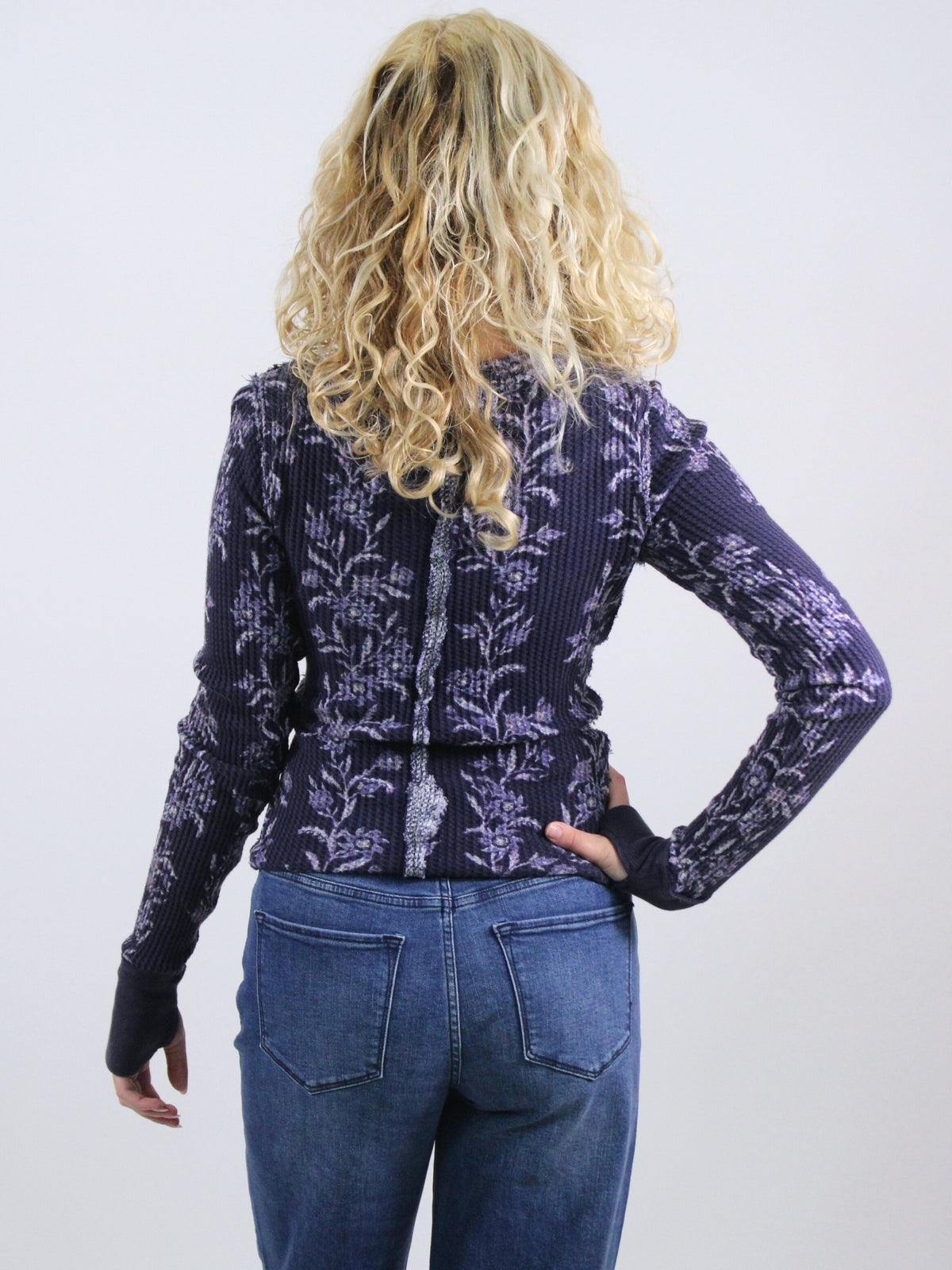 Person wearing a patterned purple sweater and blue jeans on a white background