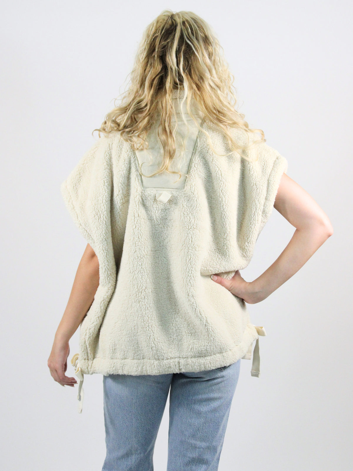 Person wearing a light-colored poncho over a shirt and jeans on a plain background