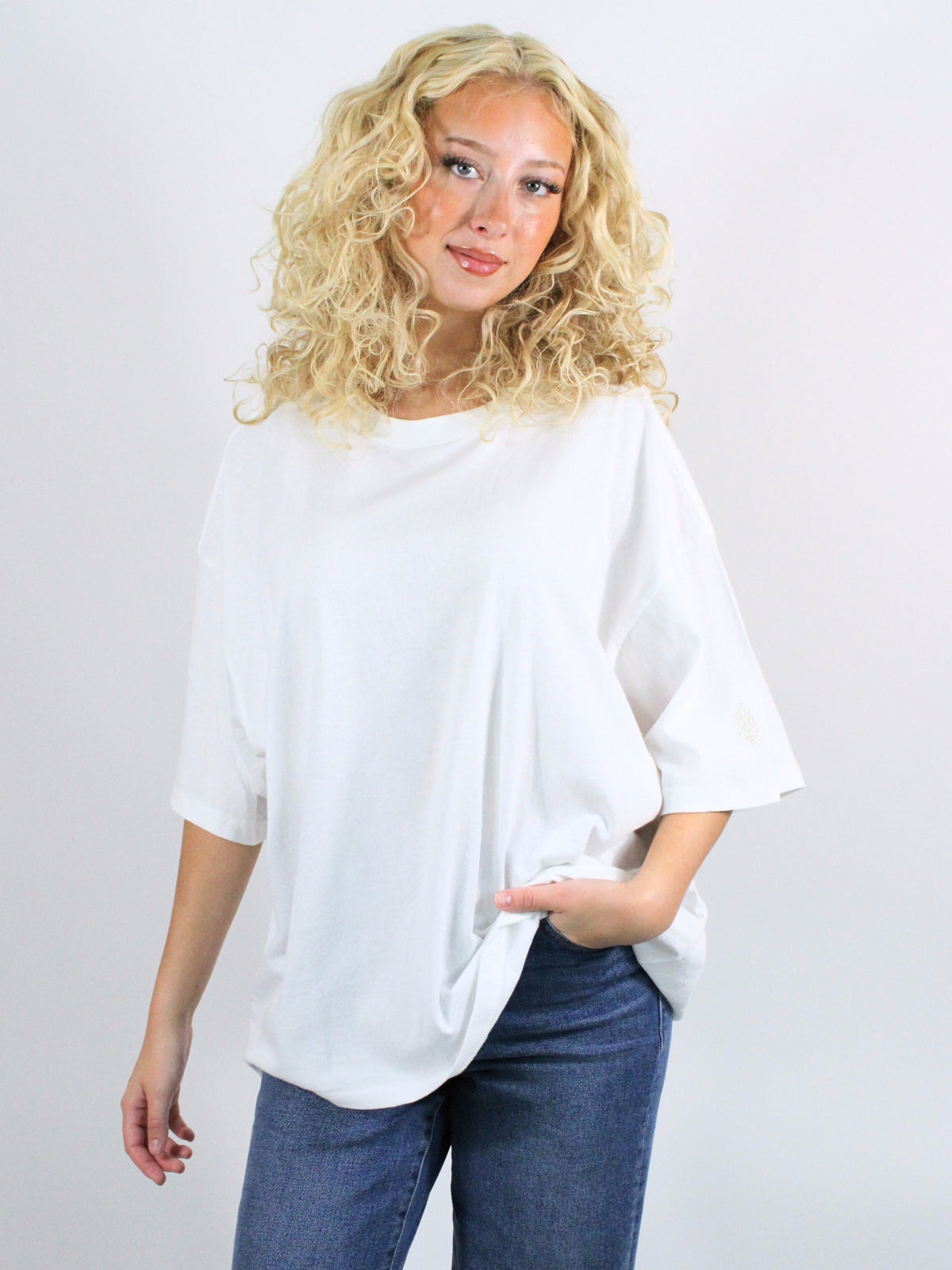 Woman wearing a white oversized shirt and blue jeans against a plain background