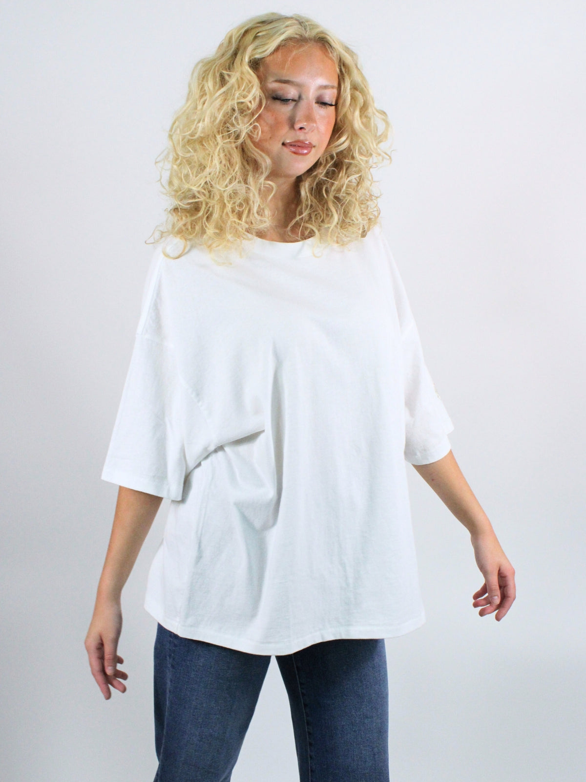 Woman wearing a white oversized shirt and blue jeans on a plain background