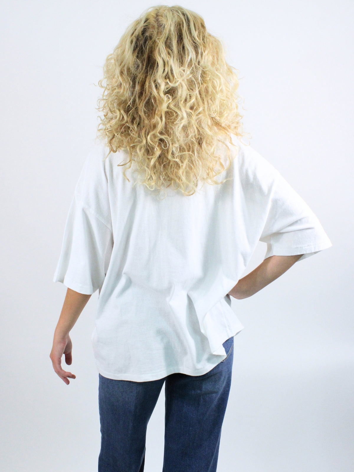 Person wearing a white oversized shirt and blue jeans on a plain background