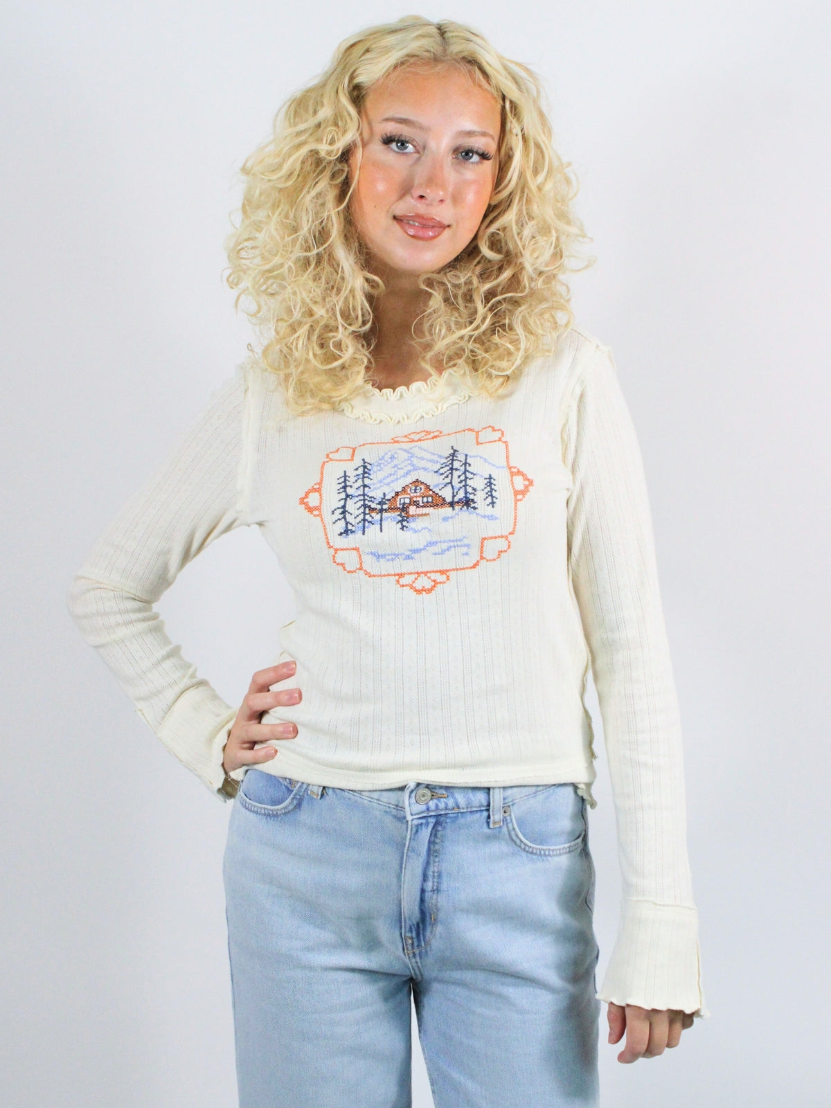 Woman wearing a cream sweater with a graphic design on a plain background