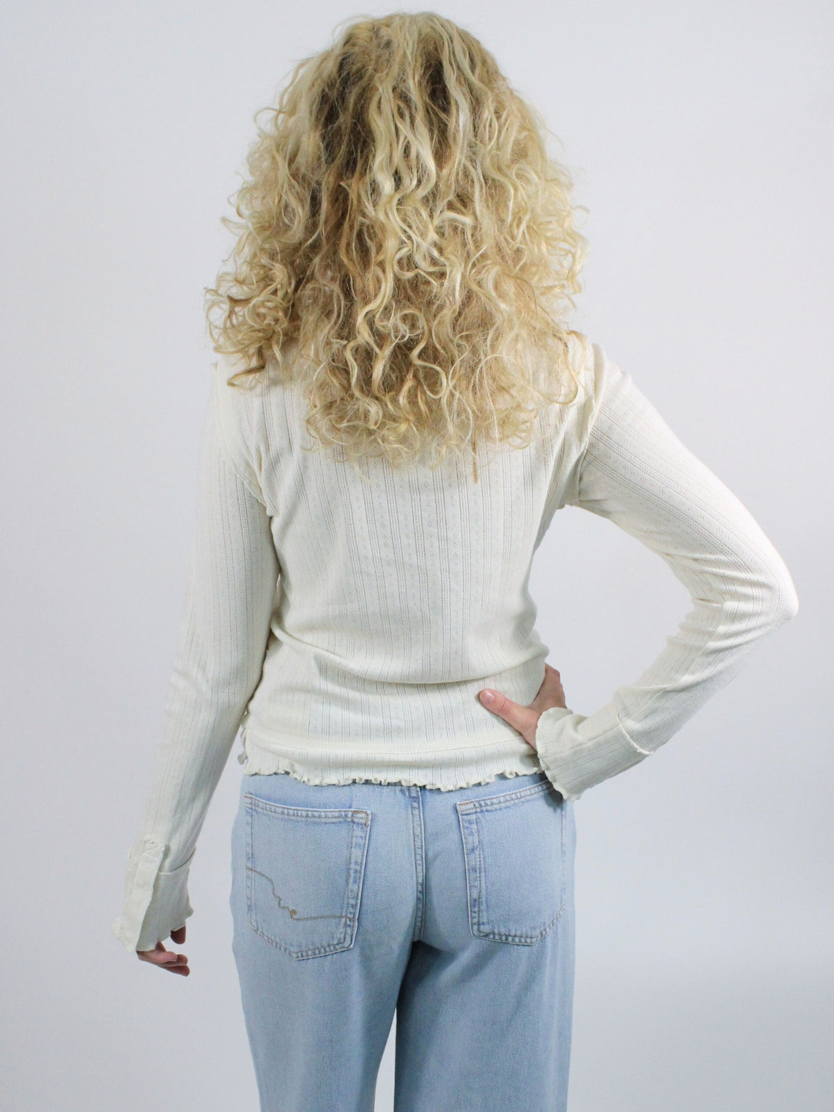Person wearing a white sweater and light blue jeans against a plain background