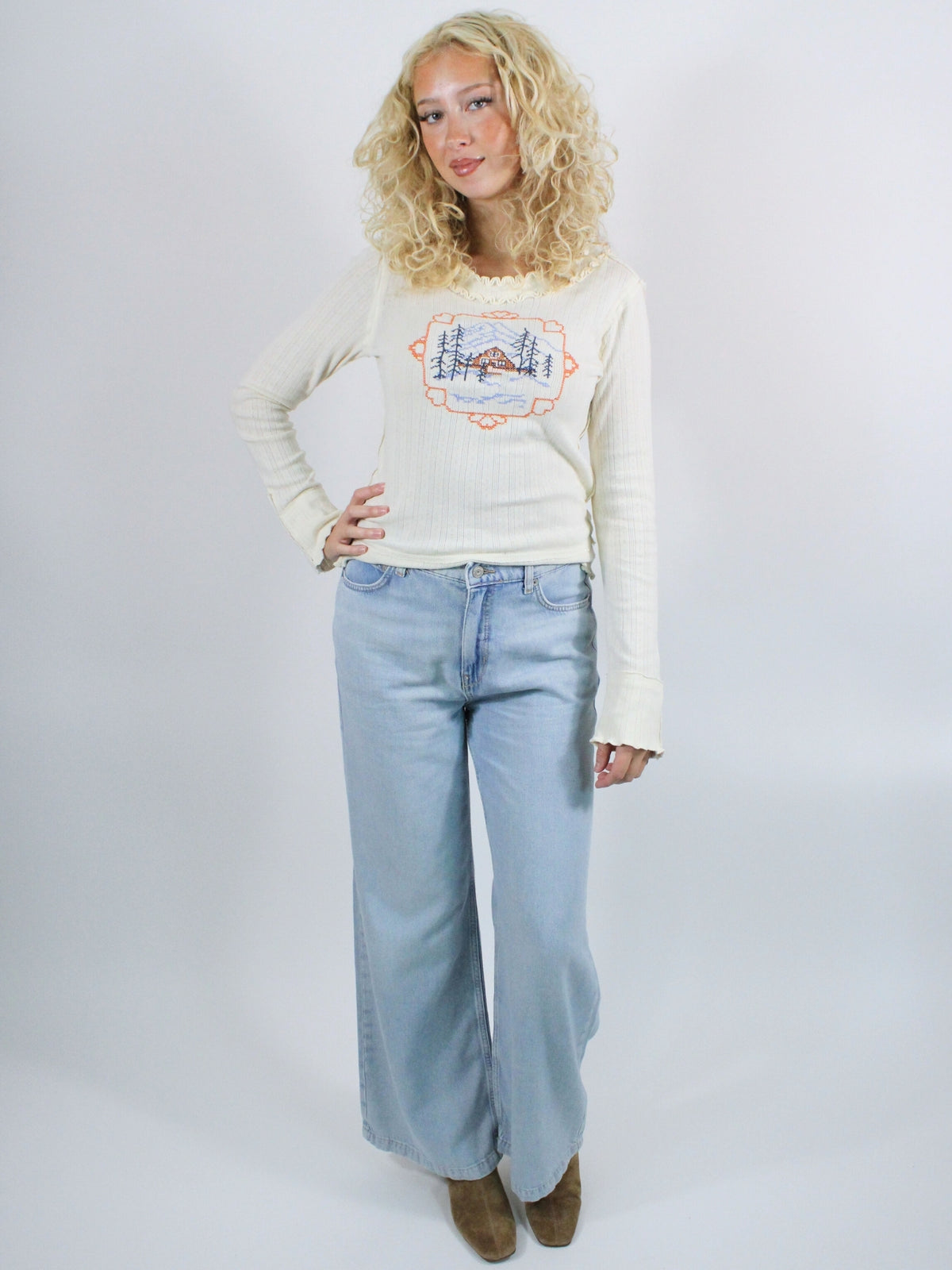 Woman wearing a cream sweater with a graphic design and light blue jeans on a white background