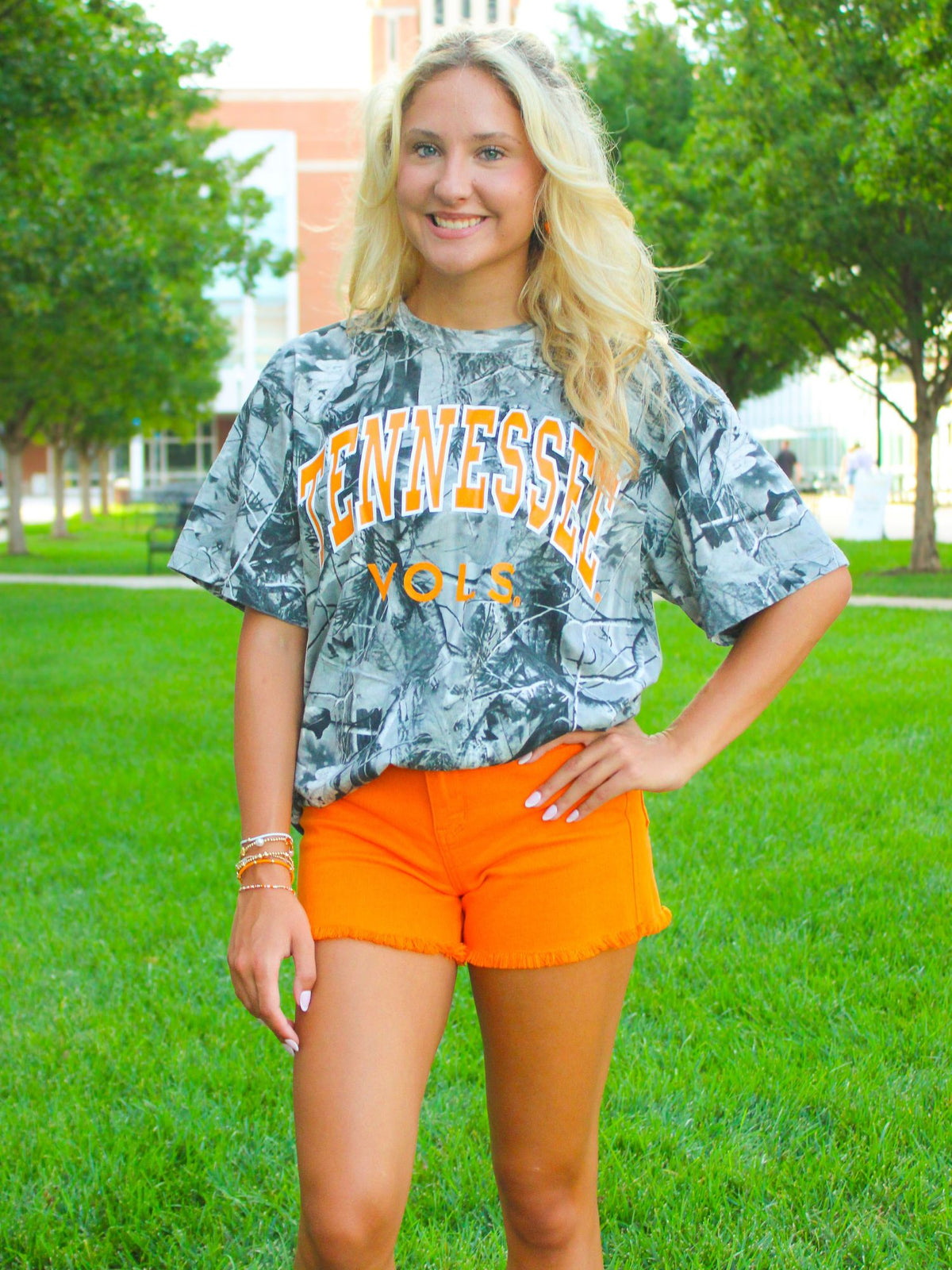 Woman wearing a Tennessee Vols shirt and orange shorts on a grassy field
