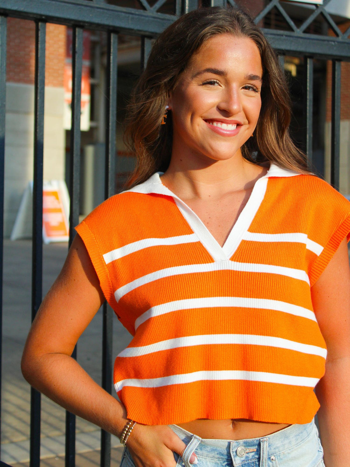 Woman wearing an orange and white striped shirt standing in front of a metal gate.