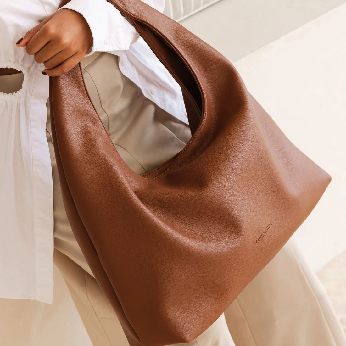 shop handbags for spring at bliss knoxville close up of model with camel leather hobo shoulder bag