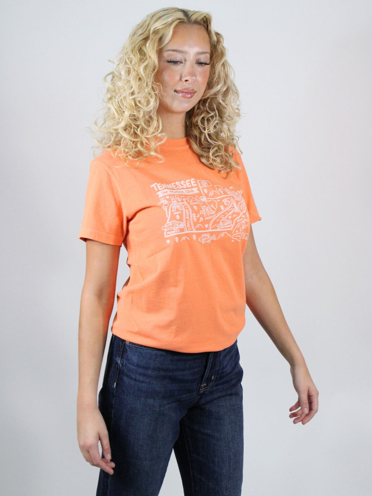 Woman wearing an orange t-shirt with text and dark jeans on a plain background