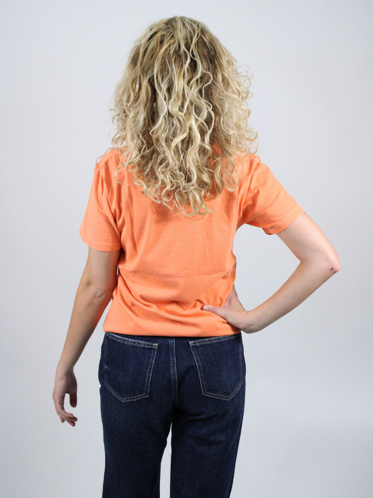 Person wearing an orange t-shirt and dark jeans against a plain background
